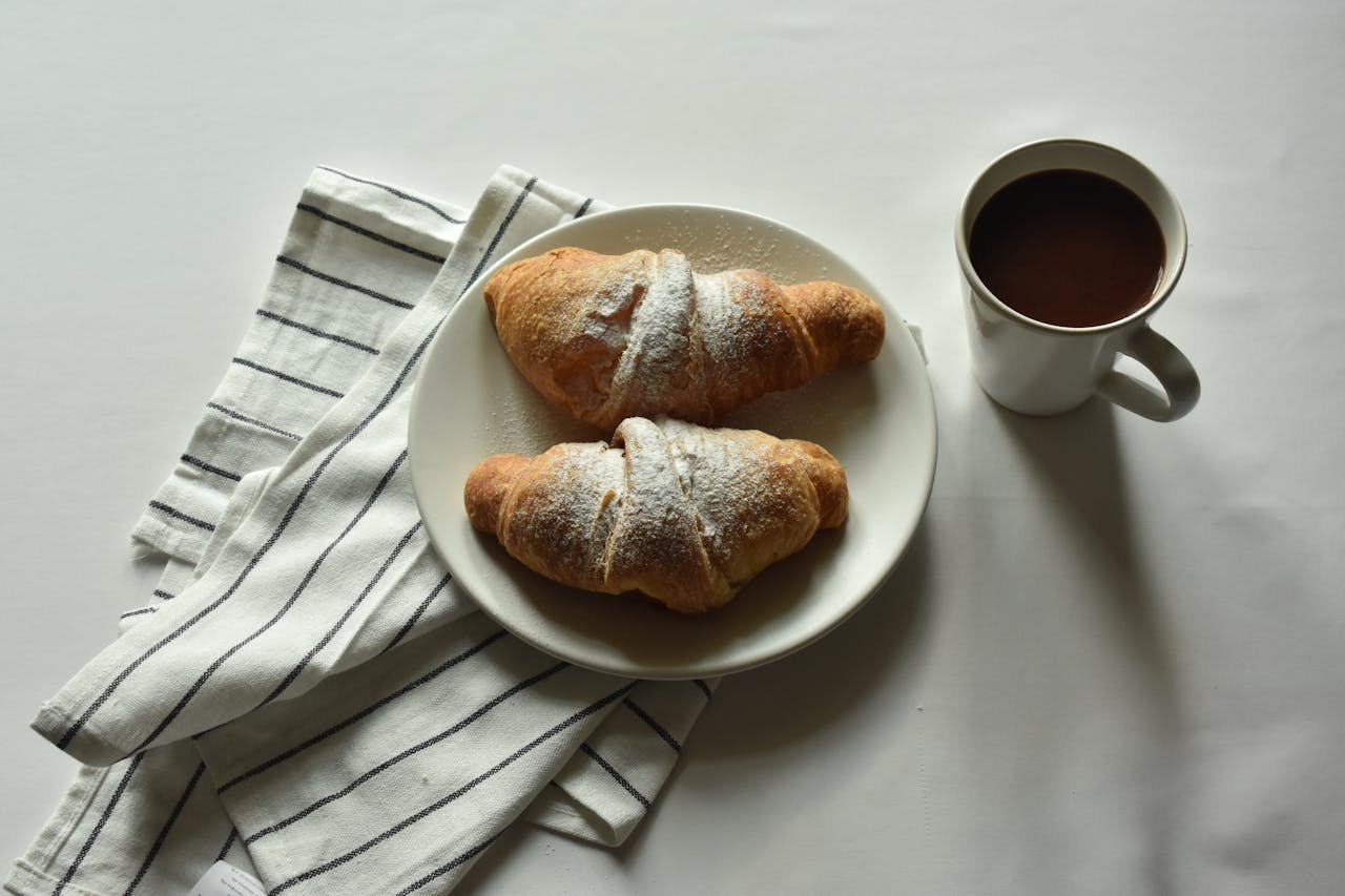 Two croissants on a plate with a cup of coffee, perfect for a cozy breakfast.
